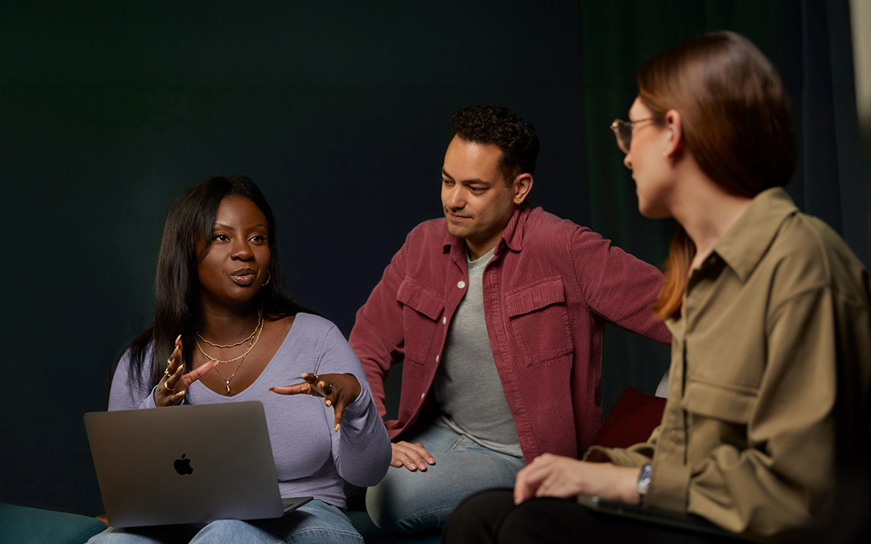 Tres personas del equipo de Servicios y Software de Apple conversan en un sillón, una de ellas con una MacBook.