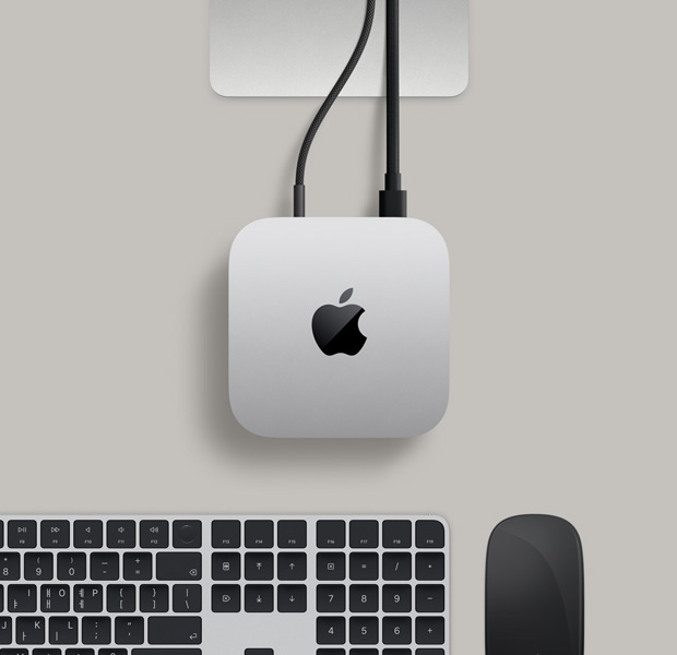 실버 색상 알루미늄 외장의 Mac mini를 위에서 바라본 모습. 둥근 형태의 모서리, 중앙의 광택 나는 검은색 Apple 로고, Studio Display 스탠드의 일부가 보입니다. Touch ID 탑재형 Magic Keyboard와 Magic Trackpad가 함께 놓여 있습니다.