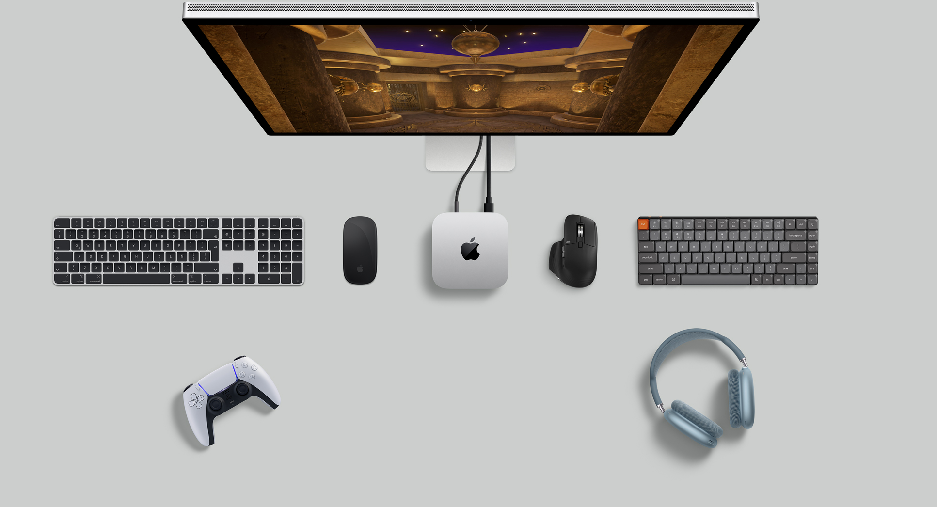 Vista desde arriba de una Mac mini color plata sobre un escritorio, con un monitor Studio Display, teclados inalámbricos, mouse inalámbricos, control para jugar y AirPods Max