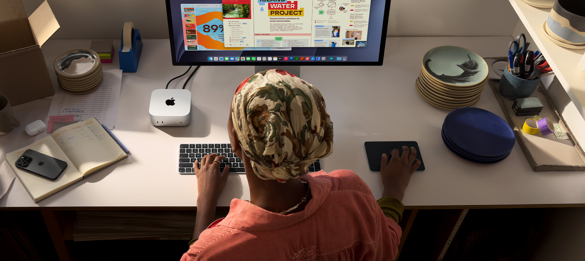 บุคคลหนึ่งกำลังพิมพ์อยู่ที่โต๊ะโดยใช้ Mac mini ที่เชื่อมต่ออยู่กับ Studio Display, Magic Keyboard, Magic Trackpad, ไอเท็มต่างๆ