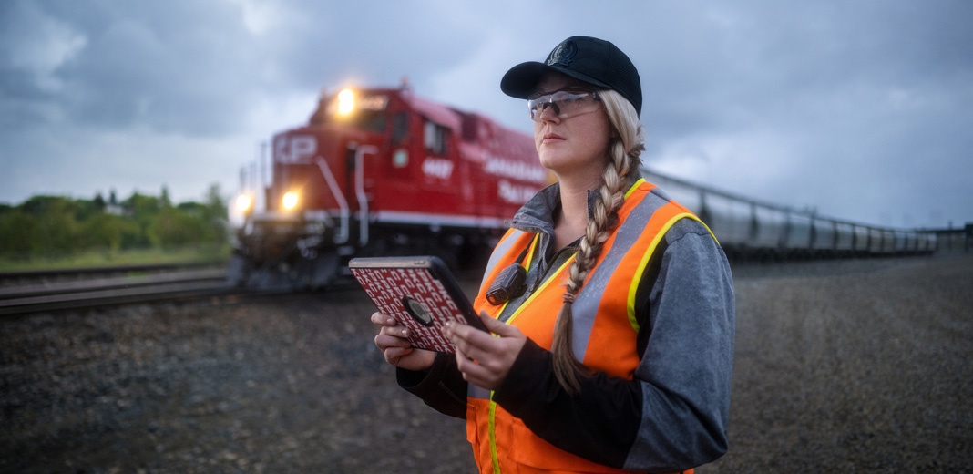 Une cheminote tenant un iPad regarde la voie ferrée au passage d’un train
