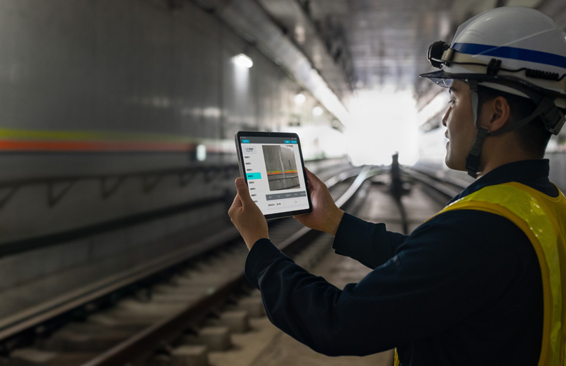 En vedligeholdelsesmedarbejder i Tokyo Metros tunneler holder en iPad op for at tage et billede af skinnerne, mens en kollega kigger på.