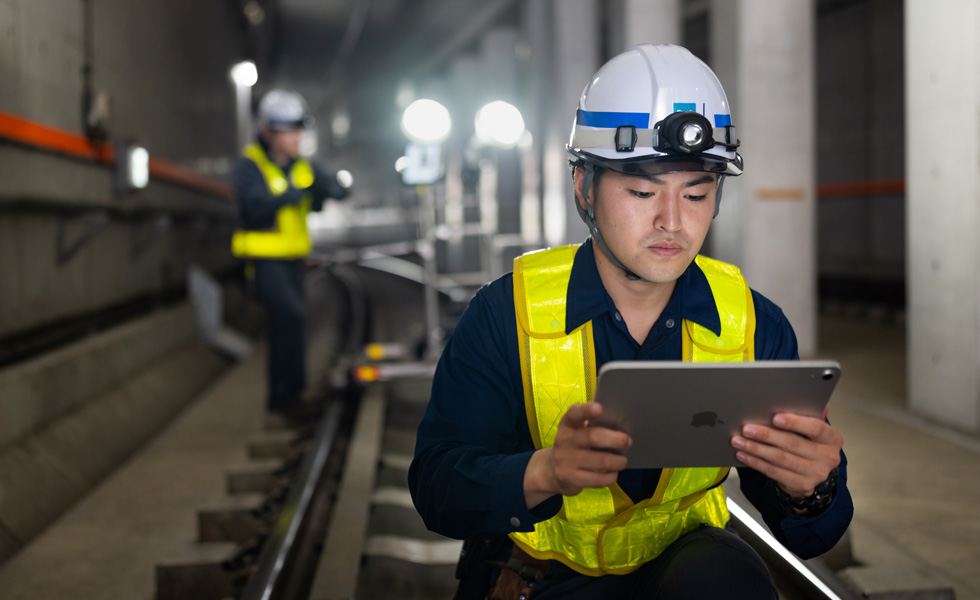 En medarbejder iført sikkerhedsvest og hjelm bruger en iPad under vedligeholdelsesarbejde i Tokyo Metros tunneler.