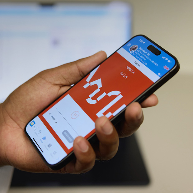 Een hand houdt een iPhone vast met daarop de Abridge-app die een gesprek tussen patiënt en arts vertaalt naar klinische aantekeningen.