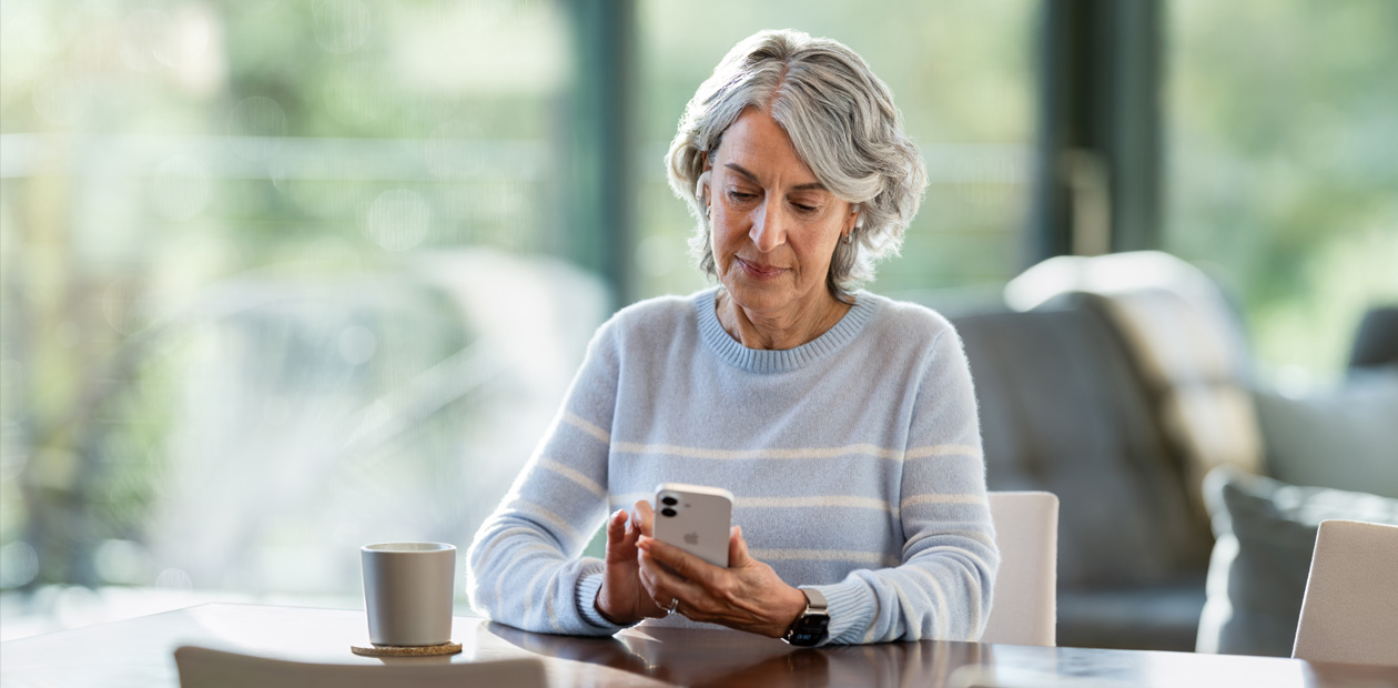 Een oudere vrouw zit aan een tafel en kijkt naar een iPhone.