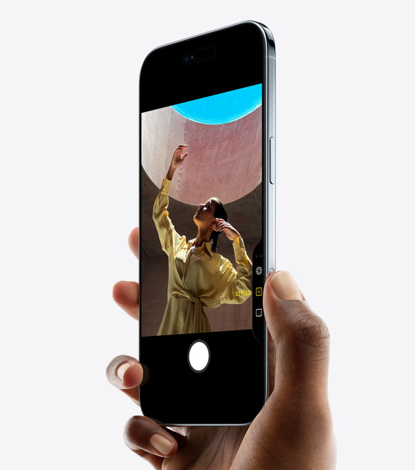 iPhone Air trzymany w dłoni z kciukiem na panelu Sterowanie aparatem, widoczny przód i bok urządzenia, jego smukły profil, Dynamic Island i przycisk boczny