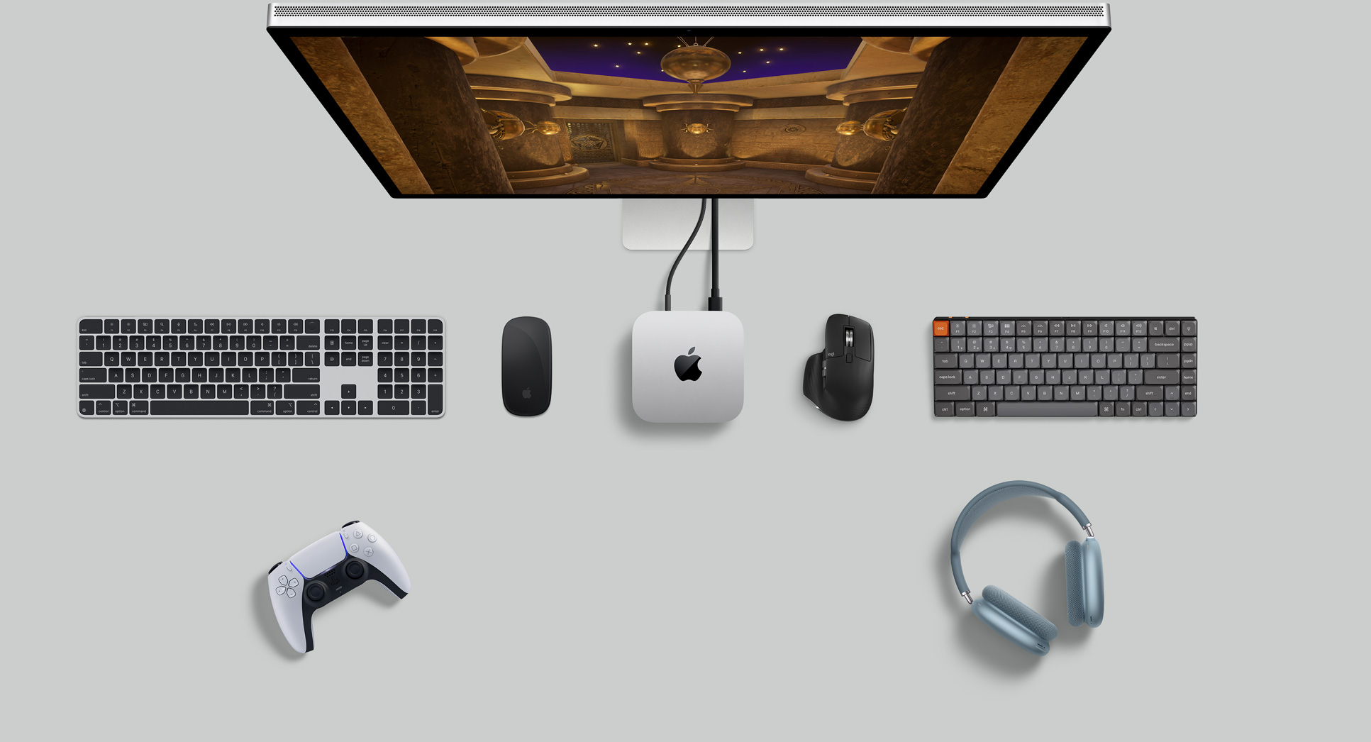 Sidabro spalvos „Mac mini“ ant stalo su monitoriumi, belaidėmis klaviatūromis, belaidėmis pelėmis, žaidimų valdikliu ir „AirPods Max“ vaizdas iš viršaus.