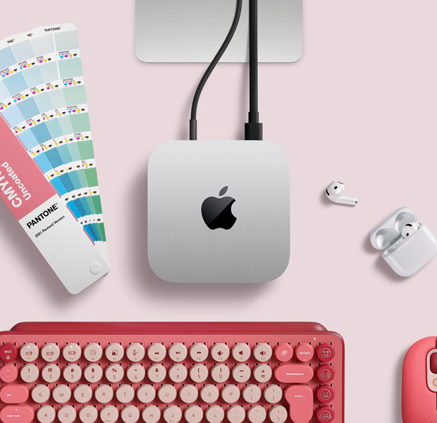 Sidabro spalvos „Mac mini“ ant darbo stalo su „AirPods“, rožine belaidžio ryšio klaviatūra, rožine belaidžio ryšio pele ir spalvų paletės vėduokle, vaizdas iš viršaus