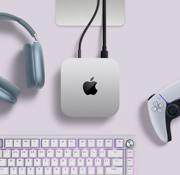 Sidabrinio „Mac mini“ su dviem laidais, prijungtais prie galinių prievadų, šalia mėlynų „AirPods Max“, sidabro spalvos klaviatūros „Magic Keyboard“ ir belaidžio žaidimų valdiklio, vaizdas iš viršaus