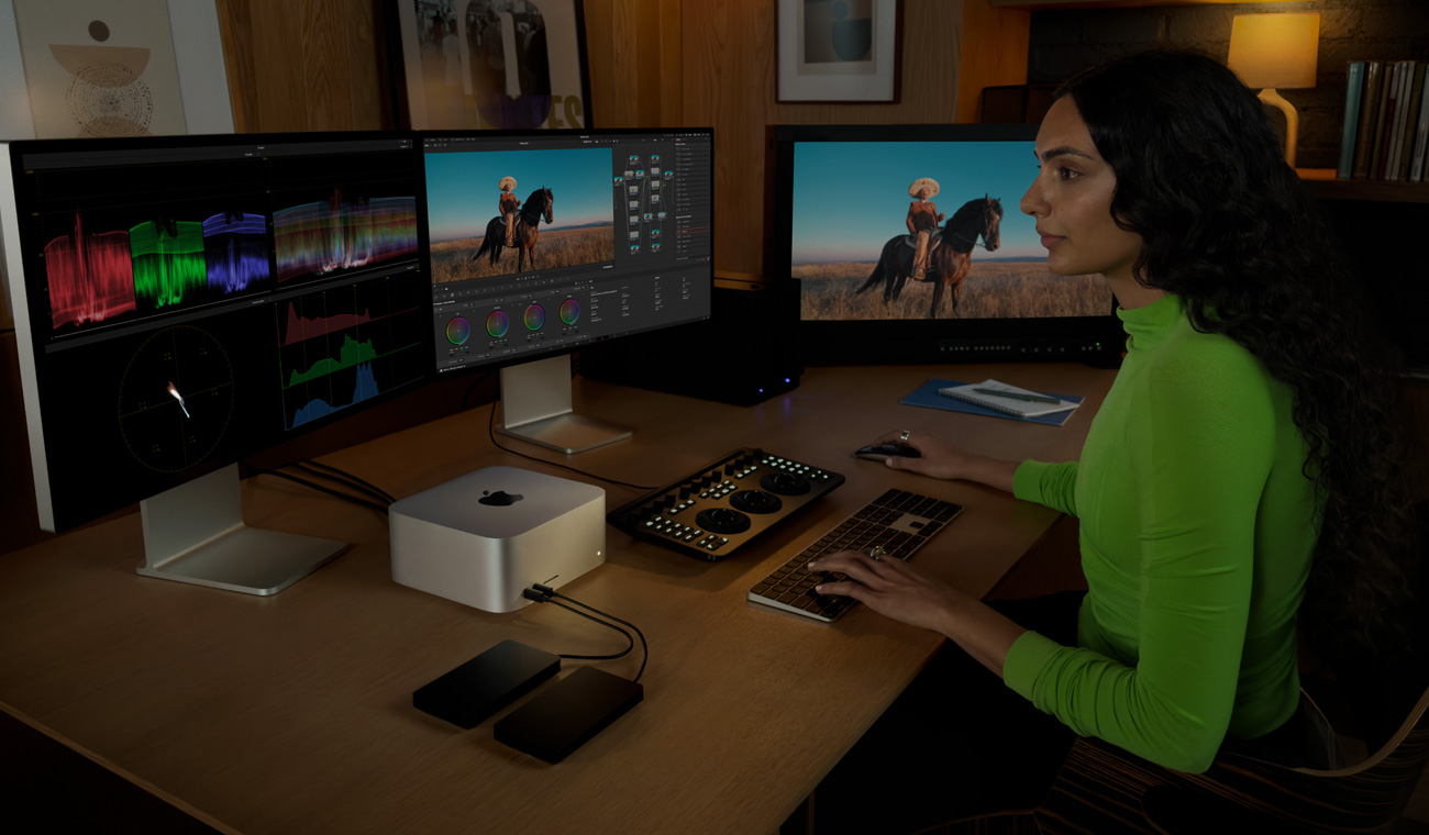 شخص محترف يعدّل ملفات باستخدام جهاز Mac Studio متصل بثلاث شاشات